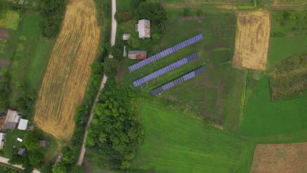 Vista aérea de arriba hacia abajo de los paneles solares en la zona rural verde cerca de los transportes en la aldea — Vídeo de stock