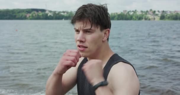 Strong boxer training kicks on open air on pond background — Stock Video