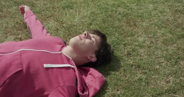 Вид на втомленого спортсмена, який відпочиває на газоні під сонцем і занурюється — стокове відео