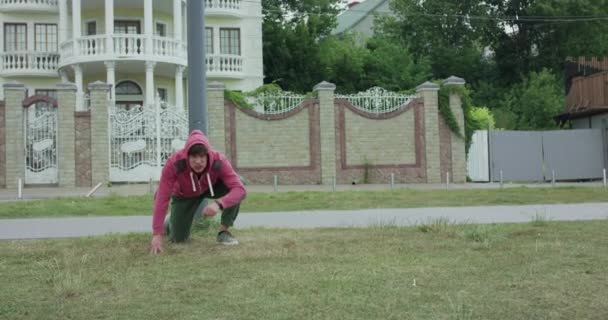 Ilska idrottsman träffar marken, står upp och träffar huvudet till pelaren och faller på gräs — Stockvideo