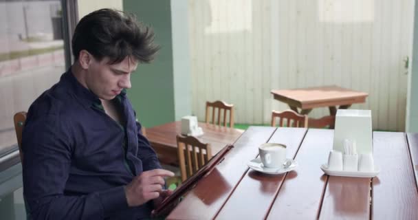 Hombre de negocios guapo sentado en la mesa en la cafetería y usando una tableta — Vídeos de Stock