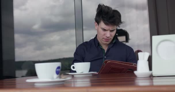 Pensativo hombre de negocios sentado a la mesa en la cafetería de la calle y usando una tableta — Vídeo de stock