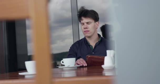 Беспокойный бизнесмен сидит в кафе, стучит по столу пальцами и пользуется планшетом — стоковое видео