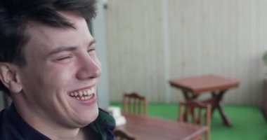 Genç adam görüntülü konuşma sırasında gülüyor ve bir fincan kahve içiyor.
