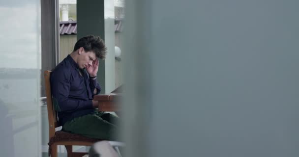 Zakenman zittend in open café, denkend en typend op een tablet in winderige dag — Stockvideo