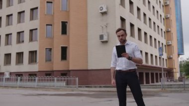 Adam durur ve siyah tabletinin üzerinde konuşur.