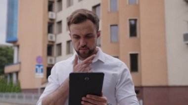 Yakışıklı adam tabletini kullanıyor ve sakalını çiziyor.