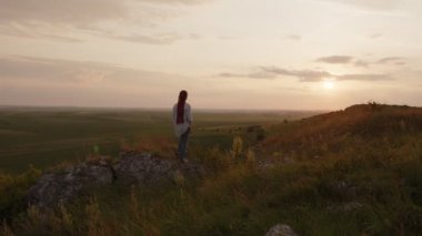 Kız gün batımına bakar ve ellerini kaldırır.