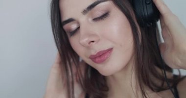 Mutlu kız kulaklık tutuyor, müzik yüzünden gözleri kapalı seviniyor, kameraya bakıyor.