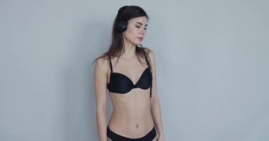 Flört eden esmer, yüzünde neşeyle bakan kulaklıkları tutuyor ve dans ediyor.