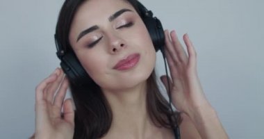 Kız kulaklıkla müzik dinliyor, gözleri kapalı ve kameraya seviniyor.
