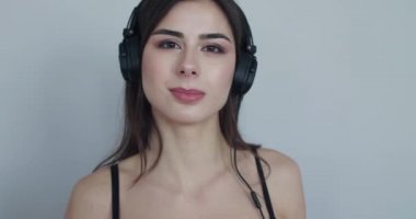 Kulaklıklı bir kız, kulaklıklara dokunuyor, kafasını sallıyor, sonra gülümsemeye başlıyor.