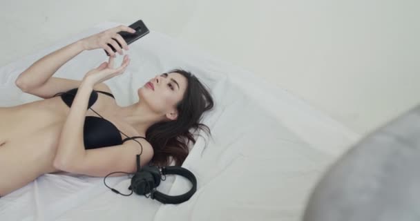 Vista dall'alto della ragazza felice in lingerie nera sdraiata sul letto e utilizzando lo smartphone — Video Stock