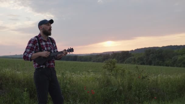 Träna man spelar på svart gitarr på grönt fält — Stockvideo