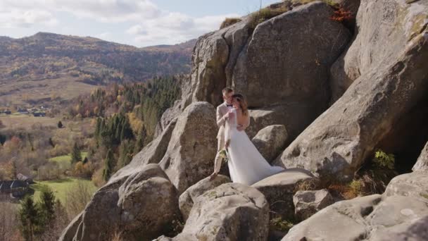 Pareja de bodas en Mountain Rock. Vista de los recién casados felices enamorados abrazándose y de pie en la cima de la montaña. — Vídeos de Stock
