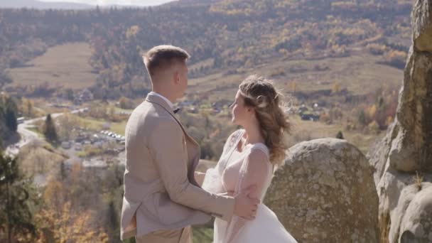 Vista lateral do rosto de um casal de casamentos na rocha da montanha. Feliz recém-casados abraçando e de pé no topo da montanha. — Vídeo de Stock