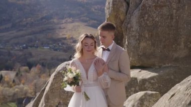 Mutlu yeni evliler dağın tepesinde kucaklaşıyorlar. Bir çift, bir kaya dağının tepesinde şefkatli duygular gösterir.