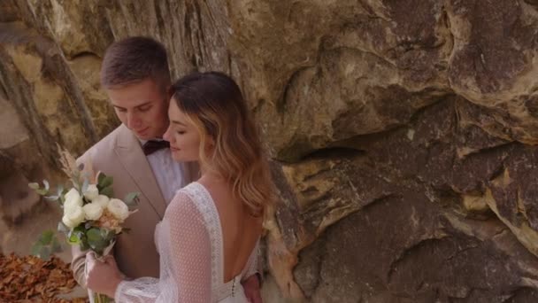 Um jovem casal nas montanhas. Recém-casados abraçando o fundo das rochas e desfrutando do buquê de casamento. — Vídeo de Stock