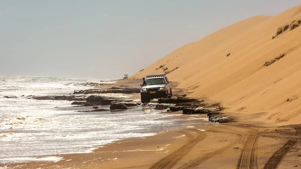 SUV off-road yapıyor, kum tepesi ve okyanus arasında. Sandviç Limanı.