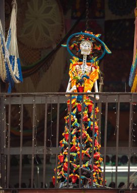  Şapkalı ve parlak Meksika elbiseli bir kadın iskeleti balkonda duruyor. Meksika 'da Ölüm Günü' nü anmak için el yapımı iskelet heykel..