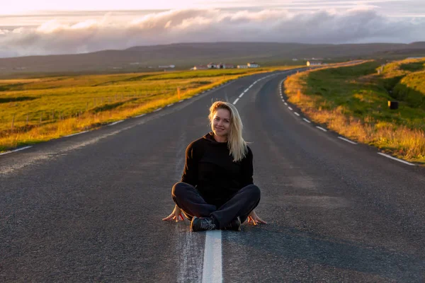 A beautiful girl is sitting on the road overlooking the Icelandic nature at sunset. Iceland