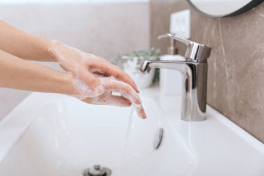 Akan su musluğunun altında ellerini yıkamak. Corona virüsünün önlenmesi için sabunla ellerini ovuşturmak, korona virüsü bulaştırmamak için hijyen. Ya da umumi tuvalette. Hijyen konsepti el detayı