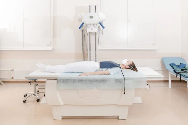 गुर्नीवर पडलेल्या रुग्णाचा क्ष-किरण घेत डॉक्टर. हॉस्पिटल रेडिओलॉजी रूम. तंत्रज्ञ एक्स-रे मशीन समायोजित करतात. बेडवर पडलेली स्त्री आधुनिक क्लिनिक ऑफिसमध्ये छाती, हृदय, फुफ्फुस स्कॅन करीत आहे — स्टॉक फोटो, इमेज