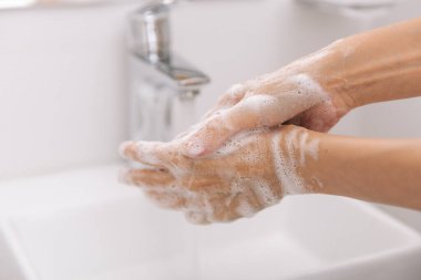 Akan su musluğunun altında ellerini yıkamak. Corona virüsünün önlenmesi için sabunla ellerini ovuşturmak, korona virüsü bulaştırmamak için hijyen. Ya da umumi tuvalette. Hijyen konsepti el detayı