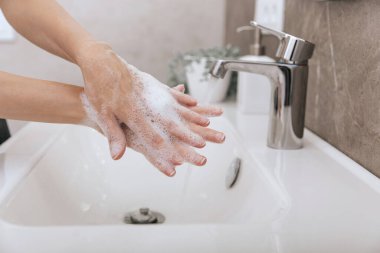 Akan su musluğunun altında ellerini yıkamak. Corona virüsünün önlenmesi için sabunla ellerini ovuşturmak, korona virüsü bulaştırmamak için hijyen. Ya da umumi tuvalette. Hijyen konsepti el detayı