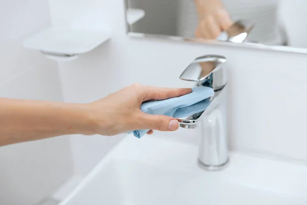 Lavabo musluğunu mikrofiber bezle temizliyorum. Banyoyu temizliyorum. Hastane ve kamusal alanlarda korona virüsüne karşı korunma yüzeylerini sterilize edin. Islak mendil kullanan kadın eli