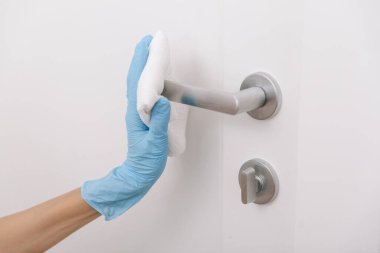Mavi eldivenli antiseptik ıslak mendille siyah kapı kolunu temizliyorum. Kadın eli temizlik için havlu kullanıyor. Hastane ve halka açık alanlarda korona virüsüne karşı yüzeylerin sterilize edilmesi