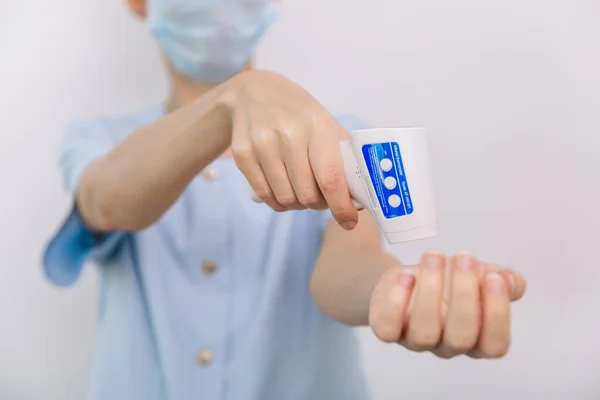 온도 측정 총을 의사의 손에 쥐고. 방어용 외과용 마스크를 착용 한 의사가 바이러스 증상을 확인하기 위해 적외선 온도계 총을 사용하는 근접 촬영 — 스톡 사진