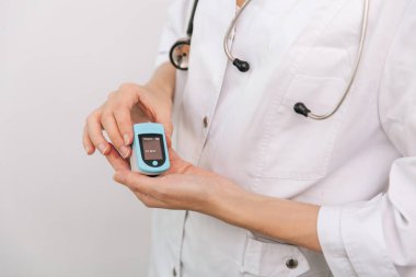 Nabız oksimetresi, beyaza izole edilmiş bir doktorun eliyle. Kişilerin oksijen doygunluğunu ölçmek için taşınabilir dijital cihaz kavramı. Oksijen doygunluğu, nabız oranı ve oksijen seviyeleri ölçülüyor.