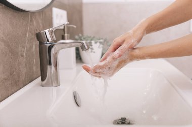 Akan su musluğunun altında ellerini yıkamak. Corona virüsünün önlenmesi için sabunla ellerini ovuşturmak, korona virüsü bulaştırmamak için hijyen. Ya da umumi tuvalette. Hijyen konsepti el detayı