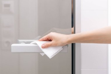 Cam kapı kollarını antiseptik ıslak mendille temizliyorum. Ev kapısı bağlantısını temizlemek için havlu kullanan kadın eli. Hastane ve halka açık alanlarda korona virüsüne karşı yüzeylerin sterilize edilmesi