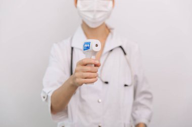 Sıcaklık ölçüm silahı doktorun elinde. Doktorun koruyucu cerrahi maske takıp vücut ısısını kontrol etmek için kızılötesi izometrik termometre tabancası kullanmaya hazır olduğu yakın çekim.