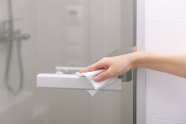 Cam kapı kollarını antiseptik ıslak mendille temizliyorum. Ev kapısı bağlantısını temizlemek için havlu kullanan kadın eli. Hastane ve halka açık alanlarda korona virüsüne karşı yüzeylerin sterilize edilmesi