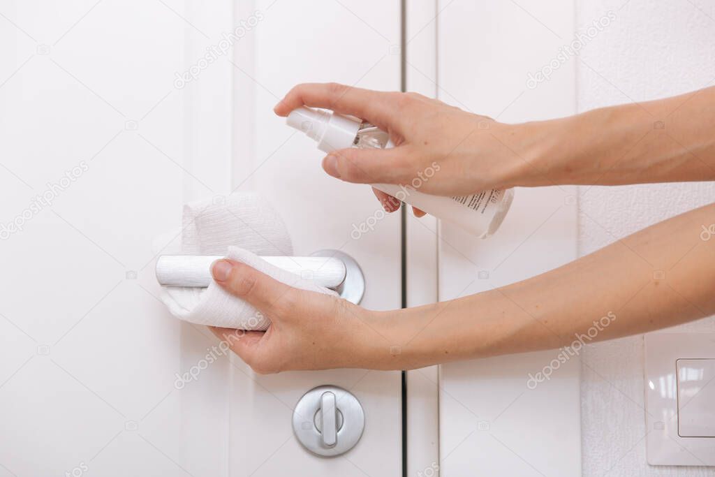 Cleaning black door handles with an antiseptic white wet wipe and sanitizer spray. Sanitize surfaces prevention in hospital and public spaces against corona virus. Woman hand using towel for cleaning