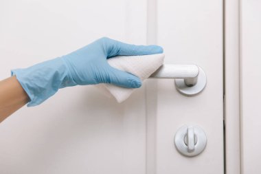 Mavi eldivenli antiseptik ıslak mendille siyah kapı kolunu temizliyorum. Kadın eli temizlik için havlu kullanıyor. Hastane ve halka açık alanlarda korona virüsüne karşı yüzeylerin sterilize edilmesi