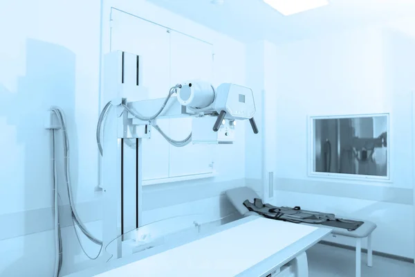 Рентгеновское отделение в современной больнице. Радиологическая комната со сканером и пустой кроватью. Техник настраивает рентгеновский аппарат. Сканирование груди, сердца, легких в современном отделении клиники — стоковое фото