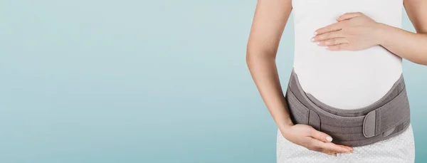 Pregnant woman belly in prenatal pregnancy maternity belt isolated on blue background. Orthopedic abdominal support waist, back, abdomen band. Belly Brace for pregnancy. Horizontal banner or poster