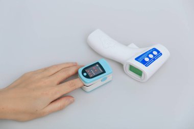 Nabız oksimetresi ve beyaz arka planda termometre tabancası. Oksijen doygunluğunu, nabız hızını ve oksijen seviyesini ölçüyorum. Virüs belirtileri için vücut sıcaklığını ölçmek için kızılötesi izometrik termometre tabancası.