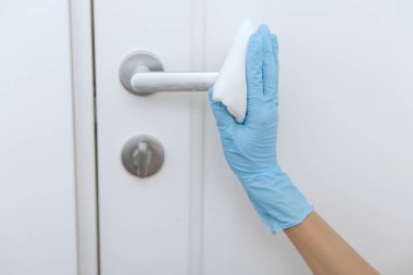 Mavi eldivenli antiseptik ıslak mendille siyah kapı kolunu temizliyorum. Kadın eli temizlik için havlu kullanıyor. Hastane ve halka açık alanlarda korona virüsüne karşı yüzeylerin sterilize edilmesi