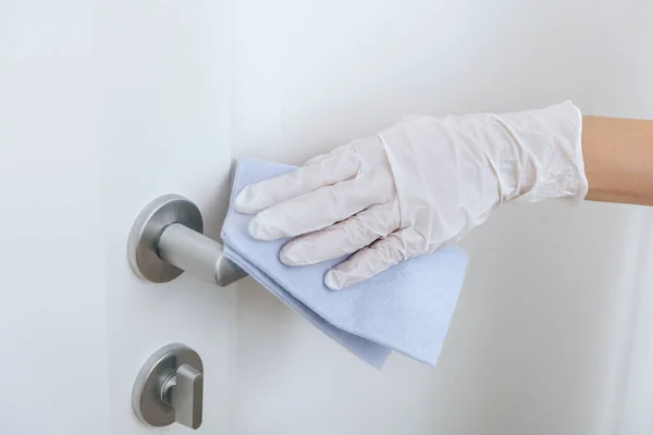 用蓝色擦拭白色手套清洁门把手.女人用毛巾清洁家房间的门链.在医院和公共场所清洁表面，防止感染日冕病毒. — 图库照片