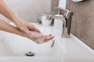 Akan su musluğunun altında ellerini yıkamak. Corona virüsünün önlenmesi için sabunla ellerini ovuşturmak, korona virüsü bulaştırmamak için hijyen. Ya da umumi tuvalette. Hijyen konsepti el detayı
