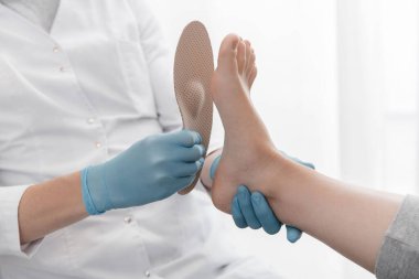 Beyaz arka planda ortopedik taban. Lastik eldivenli eller ortopedik tabanı tutuyor. Ayak bakımı, ayaklara iyi gelir. Doktor ortopedist tıbbi cihazı test ediyor. Düz taban düzeltmesi