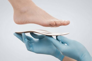 Ortopedik insole beyaz bir arkaplanda izole edildi. Lastik eldivenli eller ortopedik tabanı tutuyor. Ayak bakımı, ayaklara iyi gelir. Doktor ortopedist tıbbi cihazı test ediyor. Düz taban düzeltmesi
