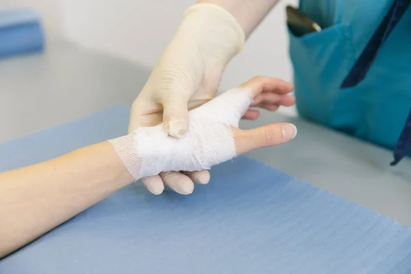 İlk yardım için bileğine dolanmış bir doktor. Hastaların ellerine bandaj uygulaması, ilk yardım konseptleri ve bilek yaralanması tedavisi. Hastanın elinde tıbbi bandaj var. Bilek ağrısı. — Stok fotoğraf