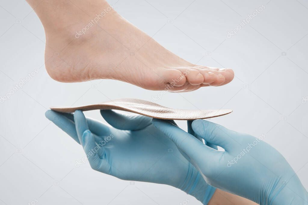 Orthopedic insole isolated on a white background. Hands in rubber gloves hold an orthopedic insole. Foot care, comfort for the feet. Doctor orthopedist tests the medical device. Flat feet correction