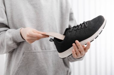 Ortopedik tabanı evde ayakkabıya takan kadın. Spor kızı ortopedik insole 'u içeride takıyor, kapat. Ayak bakımı afişi. Düz Ayak Düzeltme. Ayak hastalıklarının tedavisi ve önlenmesi
